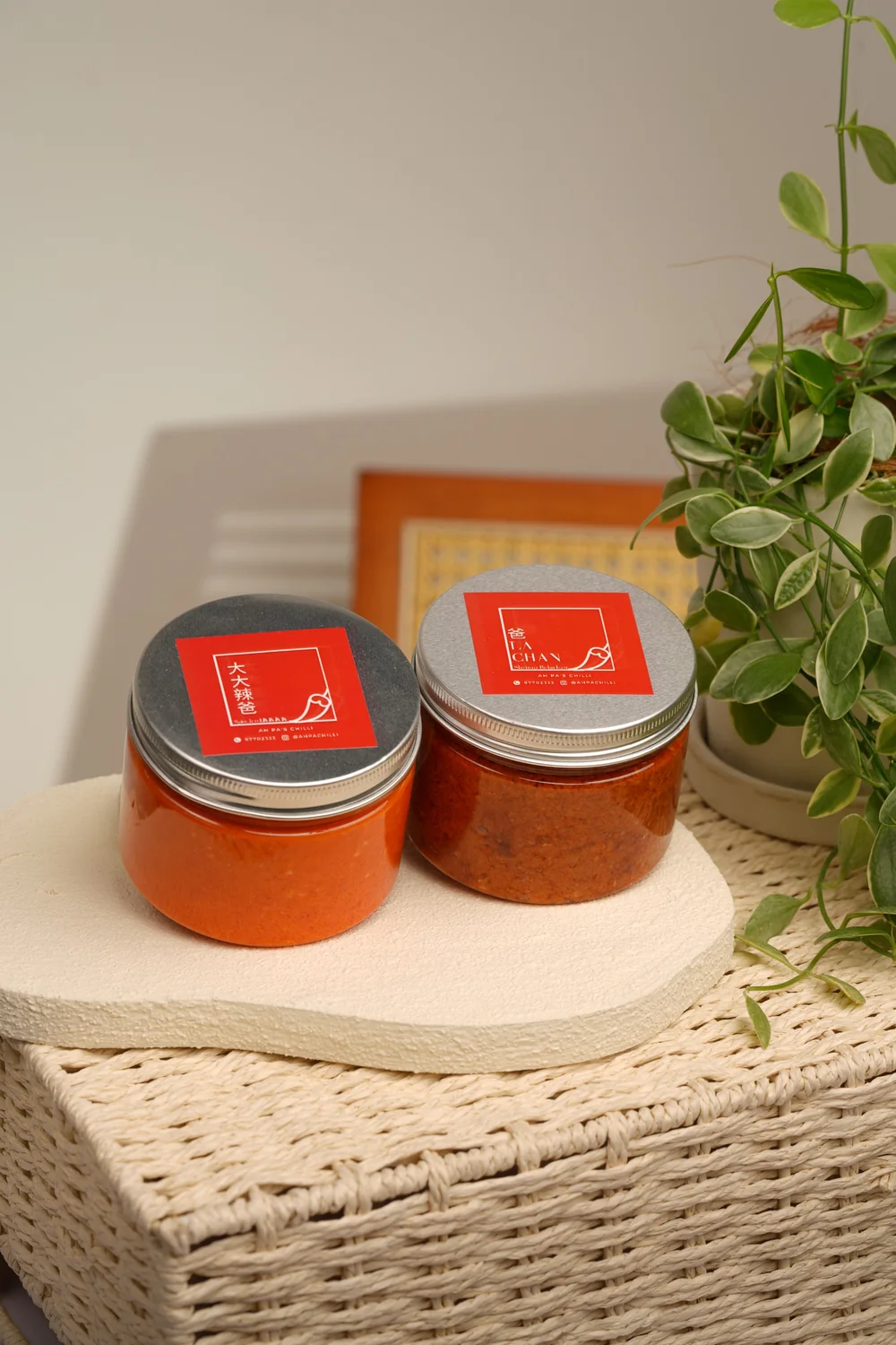 Signature chilli and Sambal Belacan jars on a woven basket at home, beside a potted plant